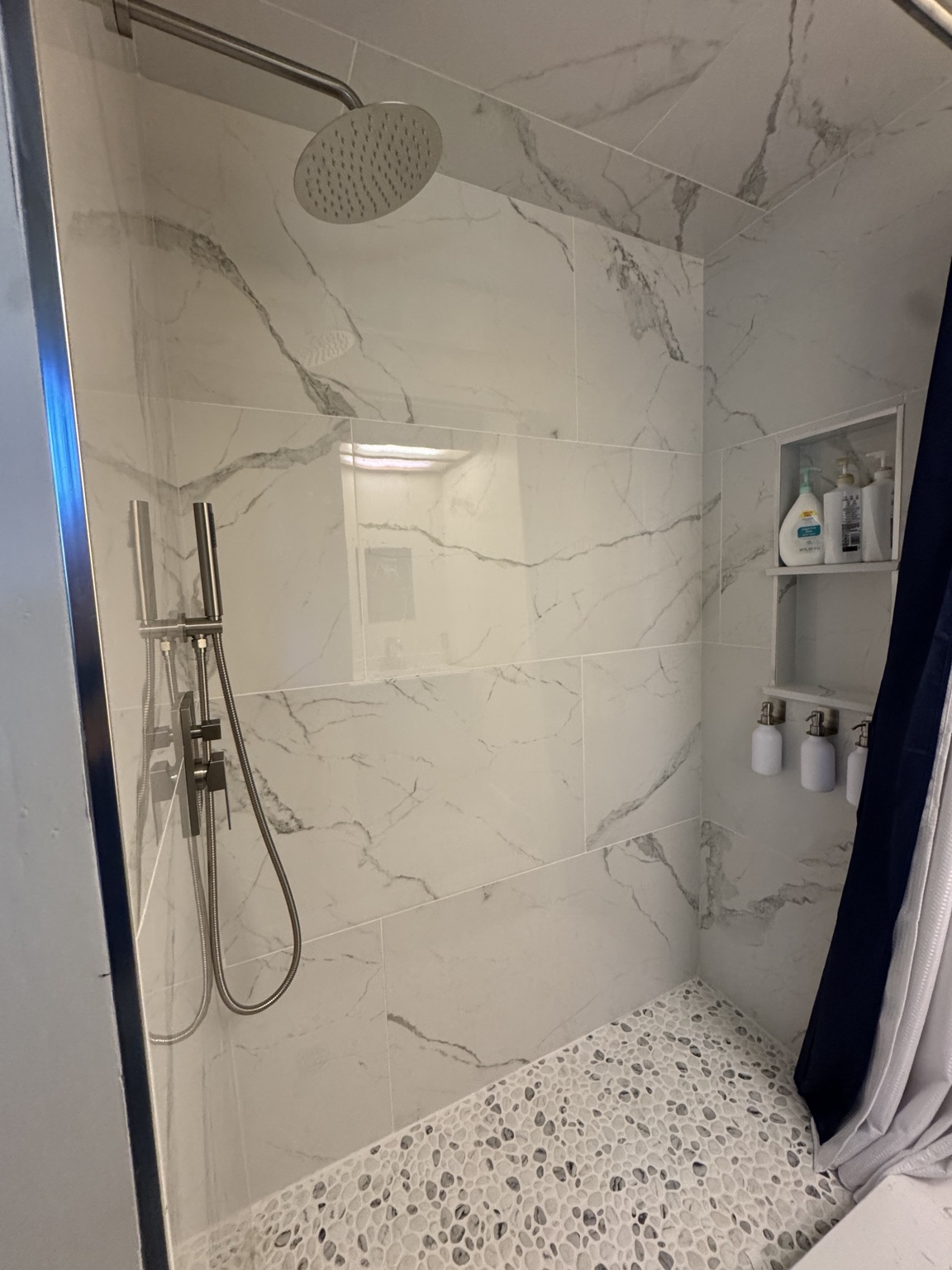 Finished walk-in shower with marble-look tile and pebble floor